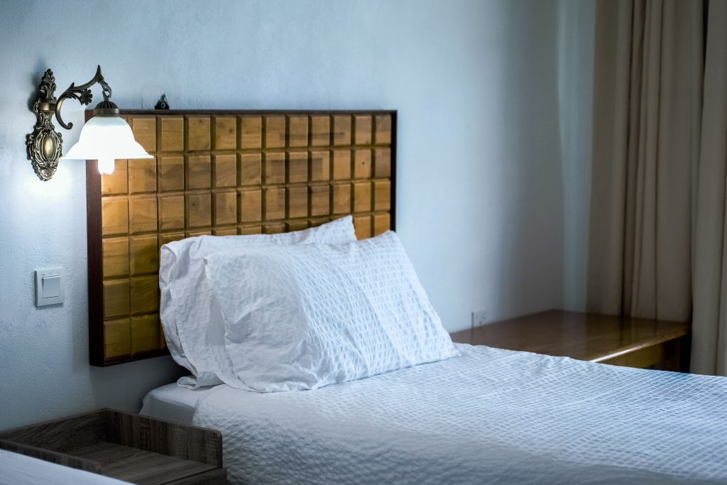 Slaapkamer met een houten hoofdbord, wandlamp en wit beddengoed