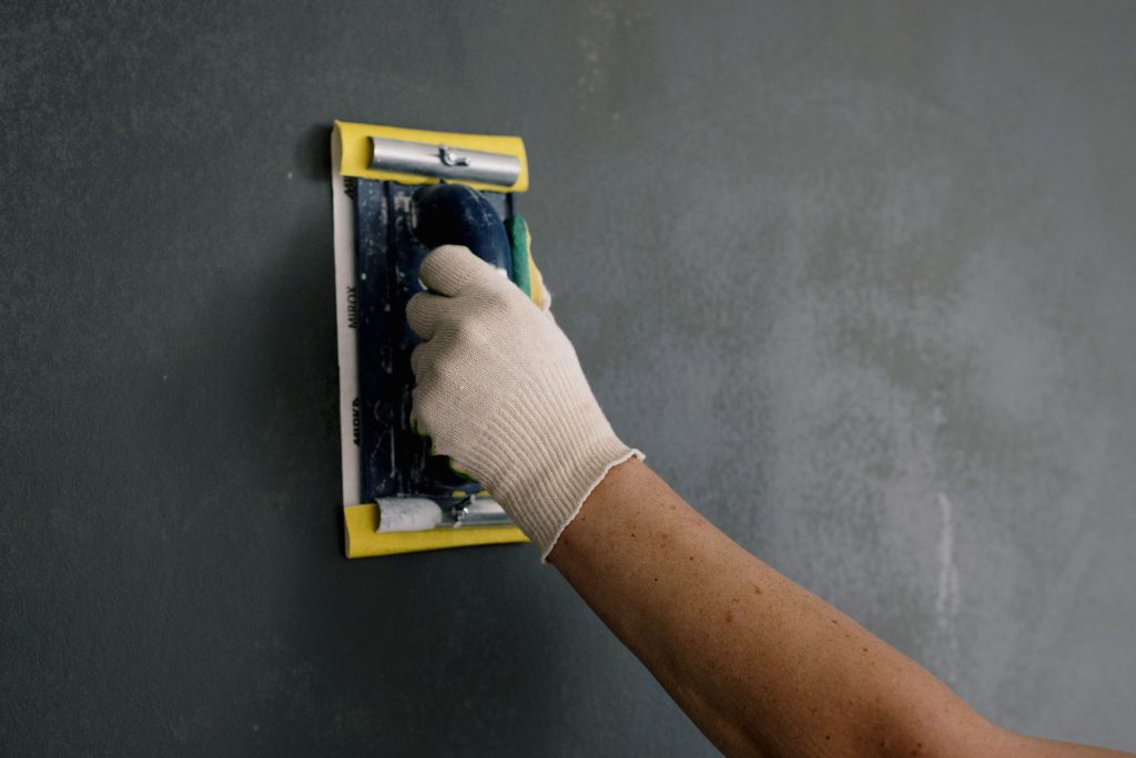 Handen met witte handschoenen en een plamuurmes bij het renoveren van een muur