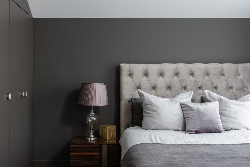 Bed met kussens naast een nachtkastje met lamp tegen een grijze slaapkamerwand