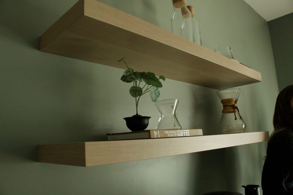 Zwevende planken met boeken, planten en karaffen aan een groene muur