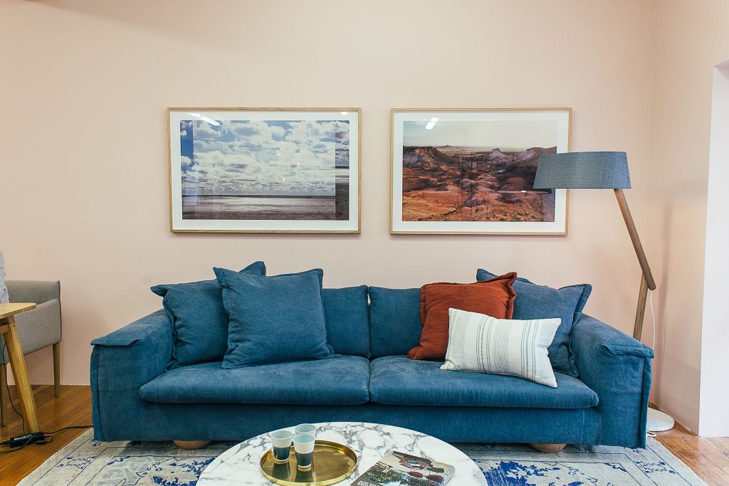 Blauwe bank met kussens en ingelijste prenten aan de muur erboven